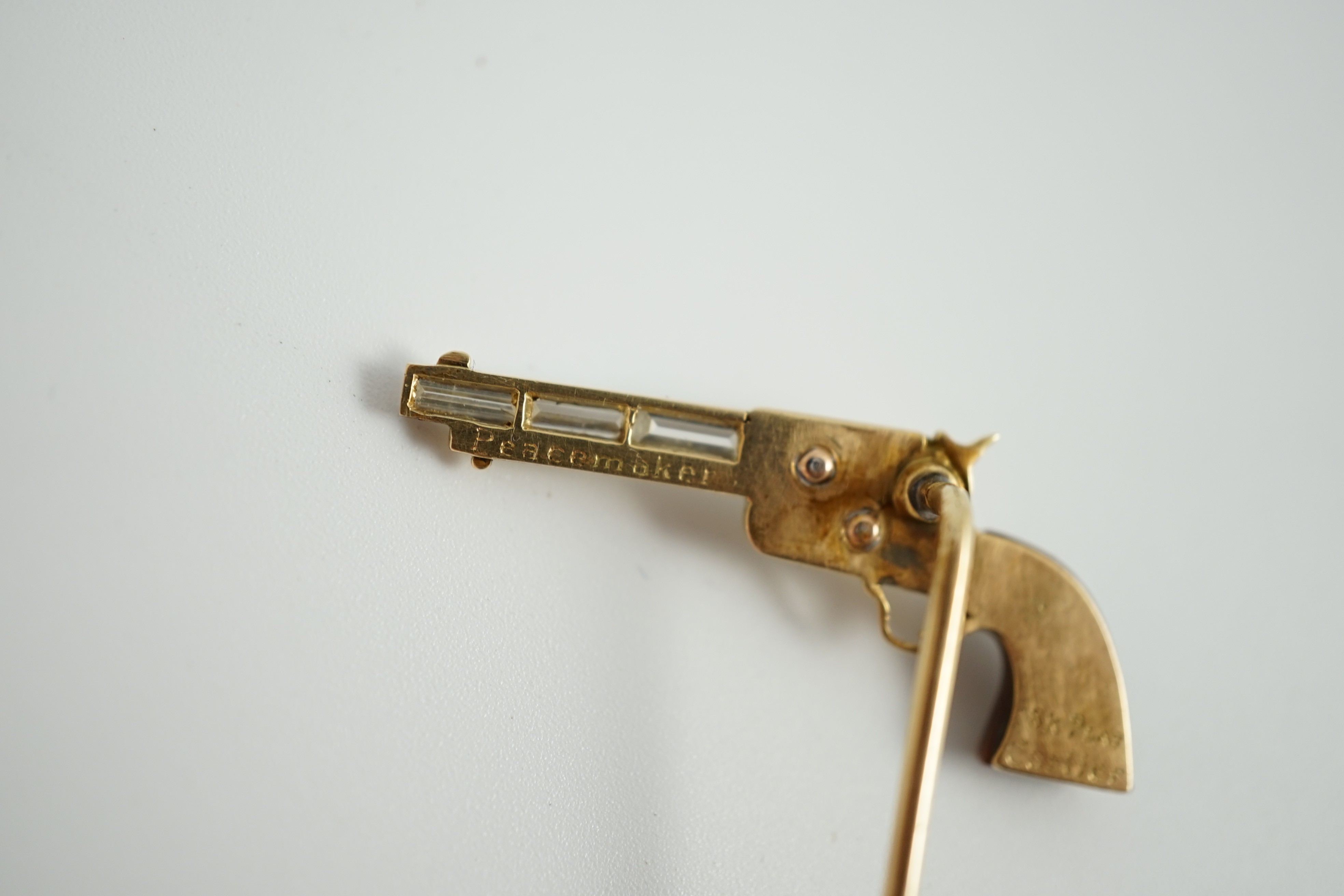 A Cartier 18k gold, platinum and six stone baguette cut diamond set novelty stick pin, modelled and a pistol inscribed 'Peacemaker'